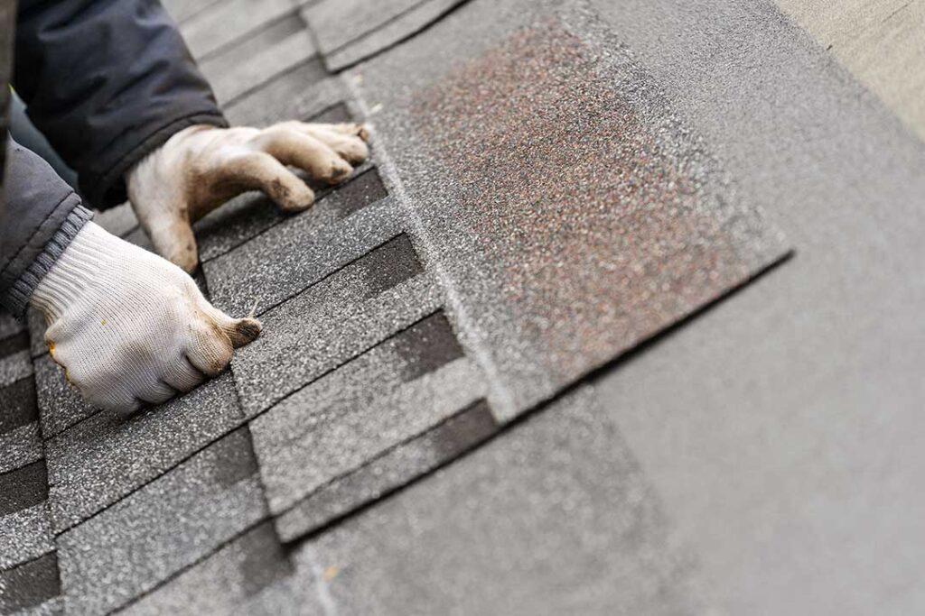 Roof shingles, flashing, and gutter debris being inspected after strong winds near a residential home.