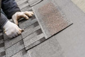 Roof shingles, flashing, and gutter debris being inspected after strong winds near a residential home.